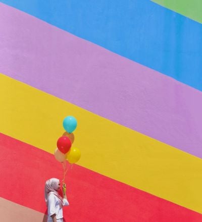 a woman holding balloons against a rainbow-themed mural