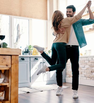 A couple dancing in the kitchen with a wide sunlit window; A couple joyfully celebrating their success in securing a rental in Los Angeles.