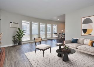 White couch with teal and orange cushions next to a marbled coffee table and a wooden chair with a cushion seat