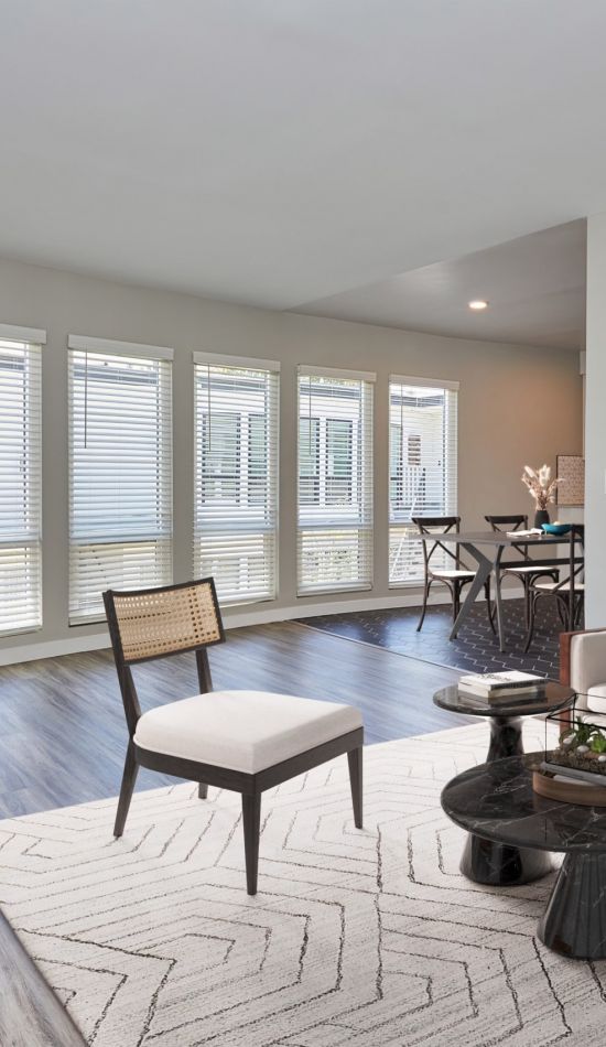 White couch with teal and orange cushions next to a marbled coffee table and a wooden chair with a cushion seat