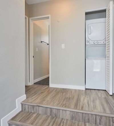 Washer and dryer stacked together in a closet at the top of two stairs.