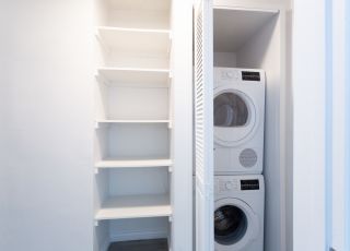 Washer and dryer stacked together on the closet next to wall shelves.