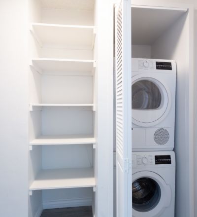 Washer and dryer stacked together on the closet next to wall shelves.