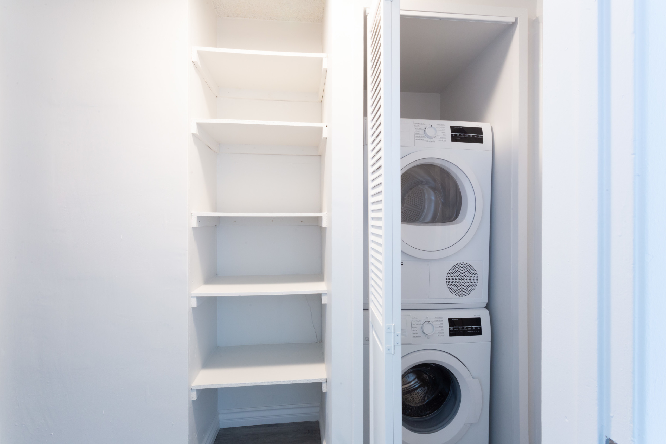 Washer and dryer stacked together on the closet next to wall shelves.