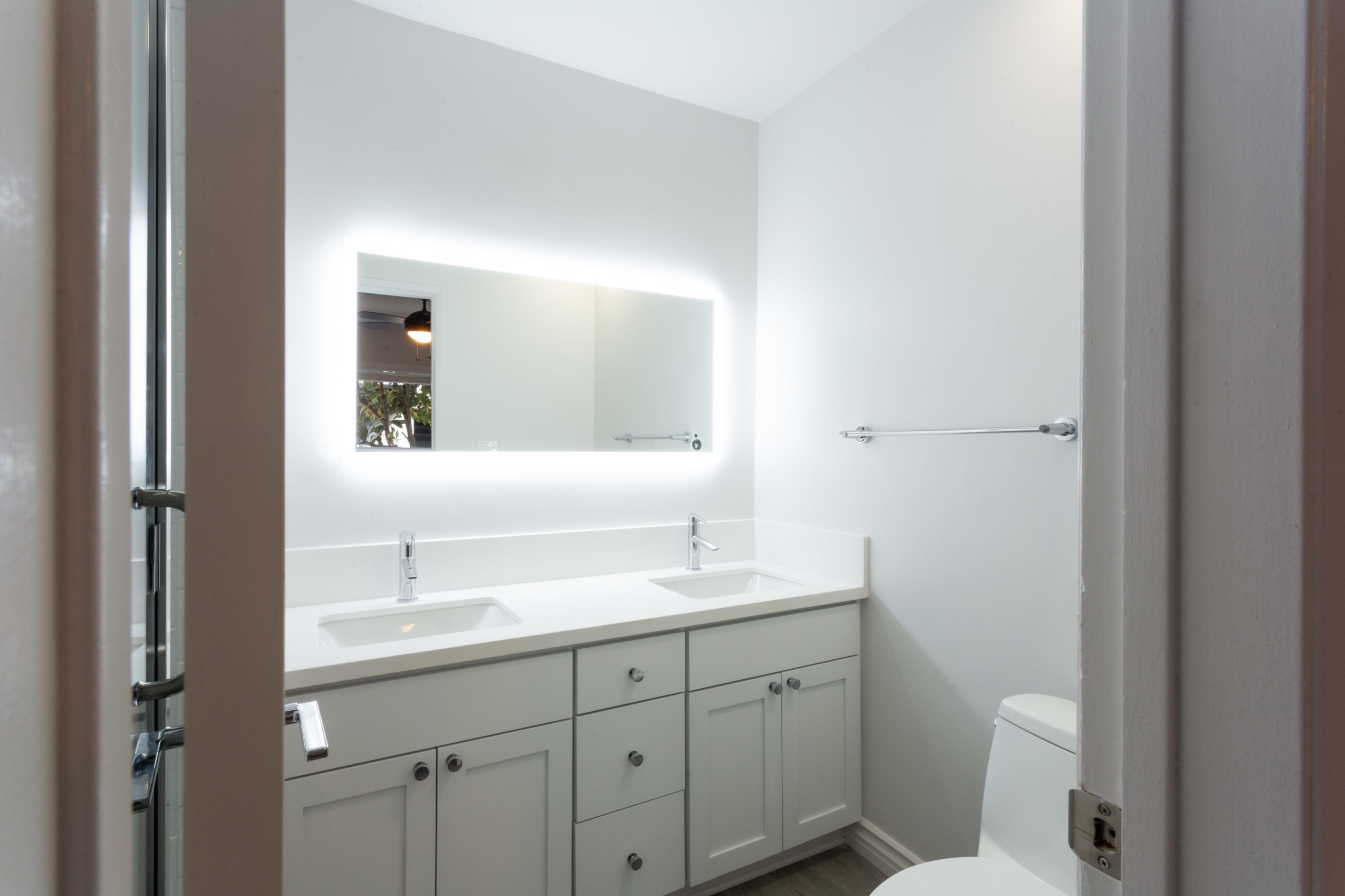 Wide backlit mirror overlooking twin bathroom sinks