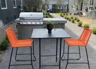 Table and two chairs on a ground level patio with a BBQ