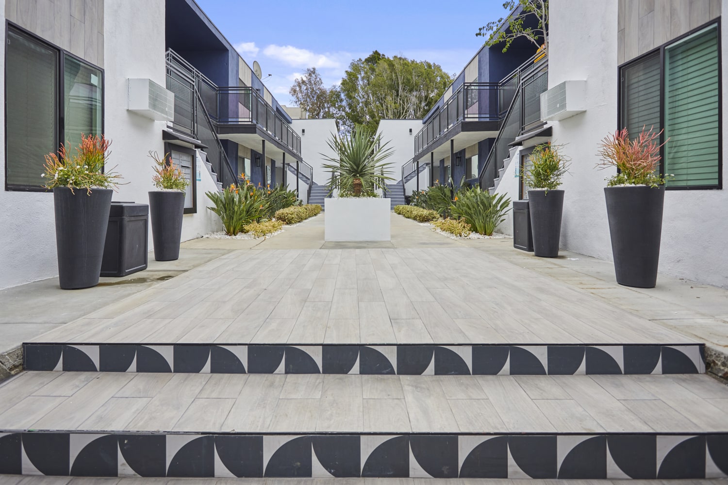 Stairs leading to the apartment courtyard decorated with potted plants on each side and a cement potted plant in the center