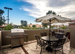 patio table with a stand umbrella next to woven chairs and bbq at Park Encino apartments