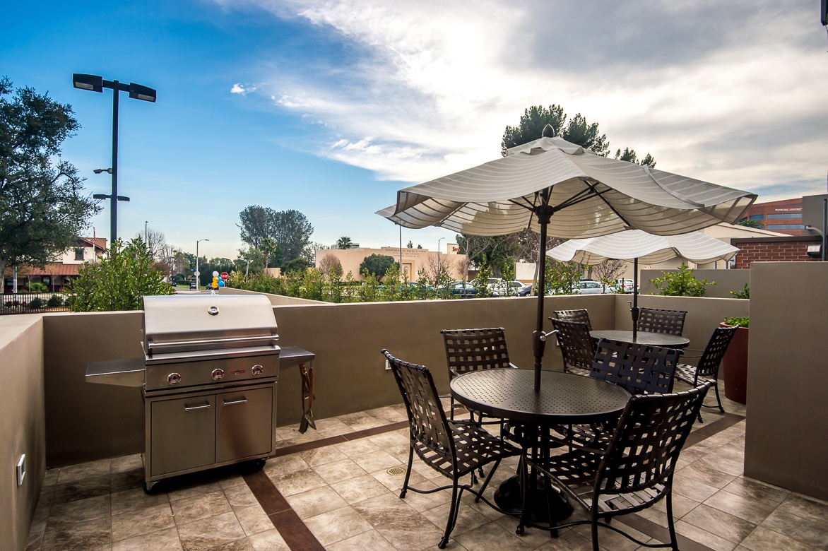 patio table with a stand umbrella next to woven chairs and bbq at Park Encino apartments