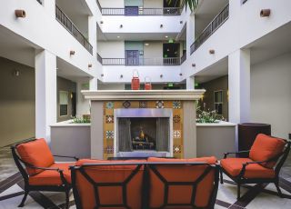 wooden patio chairs with red cushions next to an ornate fireplace at Park Encino's courtyard area