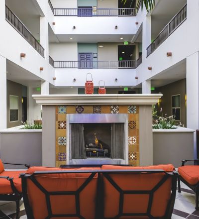 wooden patio chairs with red cushions next to an ornate fireplace at Park Encino's courtyard area