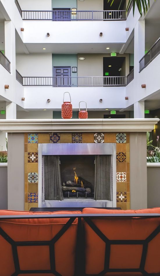 wooden patio chairs with red cushions next to an ornate fireplace at Park Encino's courtyard area