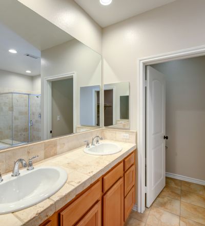 Twin bathroom sink set on a wide countertop next to a large wall mirror