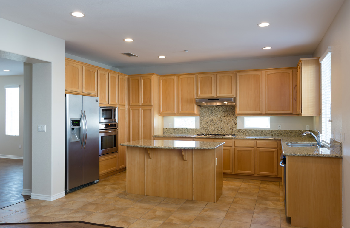 Wide kitchen countertop with wooden cabinets next to a double fridge and microwave and oven