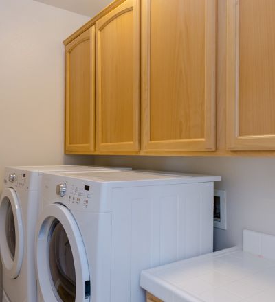 Laundry room with washer and dryer lined together and wooden cabinets on the top