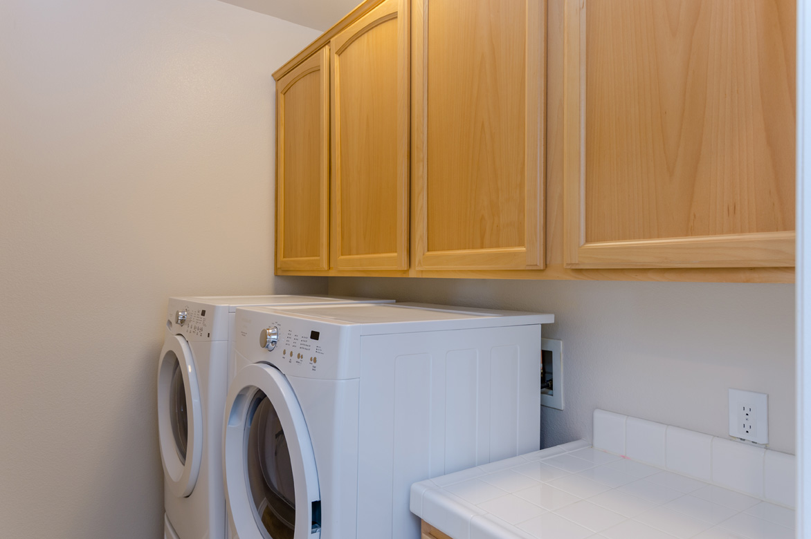 Laundry room with washer and dryer lined together and wooden cabinets on the top