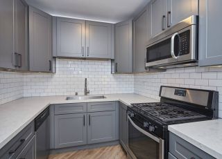 Marble kitchen countertop with grey cabinets including stainless steel microwave and oven