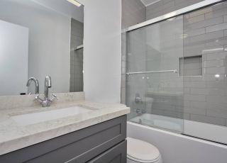Apartment bathroom with marble countertop and dark-washed cabinet next to the toilet and glass-framed bathtub