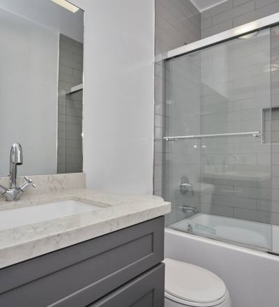 Apartment bathroom with marble countertop and dark-washed cabinet next to the toilet and glass-framed bathtub
