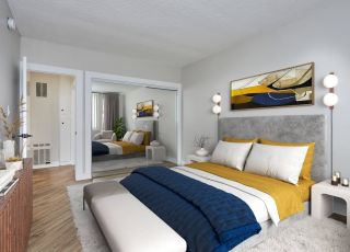 Spacious bed with duvet and pillows and a velvet headboard next to a mirror slider closet and a dresser in the front