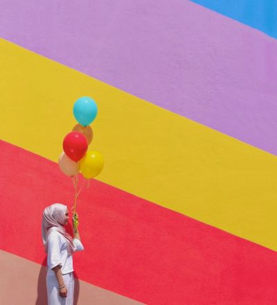a woman holding balloons against a rainbow-themed mural