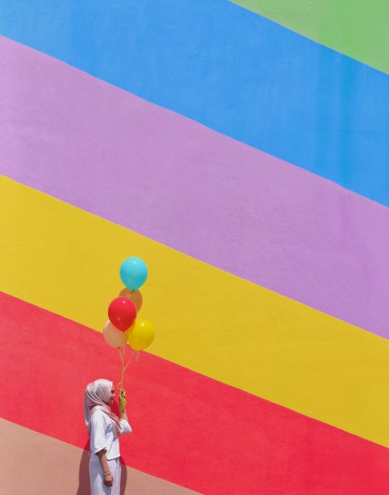 a woman holding balloons against a rainbow-themed mural