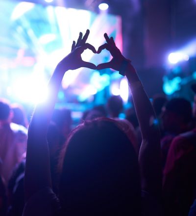 a concert with someone making a heart with hands in the foreground
