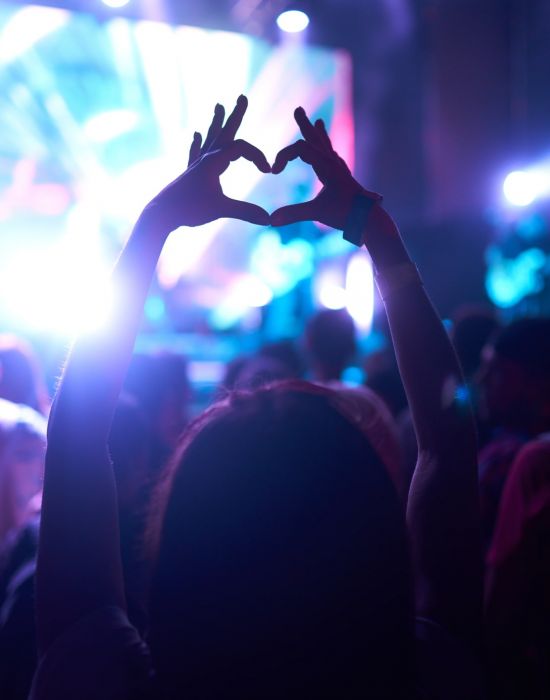 a concert with someone making a heart with hands in the foreground