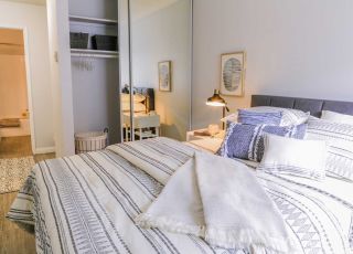 ViveLA Violet on Virgil; Bed with tufted headboard, pillows and duvets next to a mirror slider closet