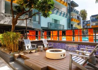 Communal fire pit in between wooden patio chairs next to the outdoor pool at Violet on Virgil Apartments