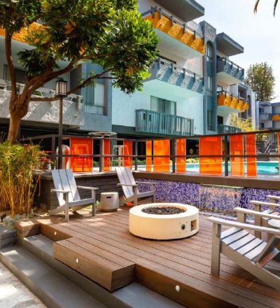 Communal fire pit in between wooden patio chairs next to the outdoor pool at Violet on Virgil Apartments