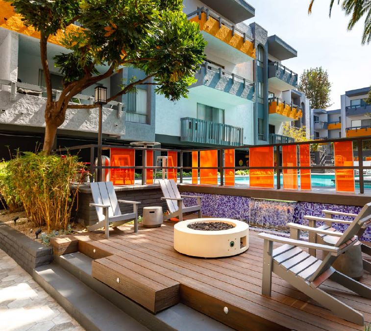 Communal fire pit in between wooden patio chairs next to the outdoor pool at Violet on Virgil Apartments