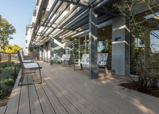 Violet on Virgil Apartments patio with a wooden deck and iron benches next to garden beds
