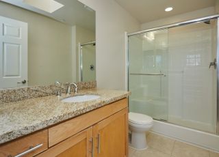 Wall mirror next to a wide marble-finished bathroom countertop with cabinets beside the toilet and glass-enclosed stall