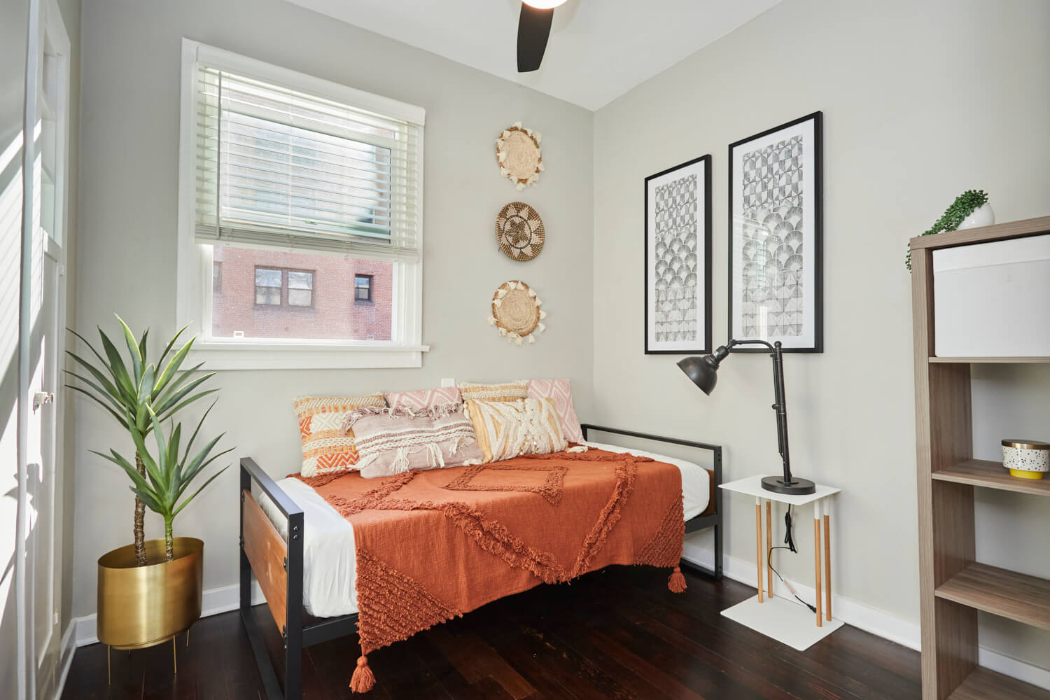 Single bed with an orange throw and pillows next to a sunlit window; Luxury Hollywood Rentals; boutique community apartments in Hollywood