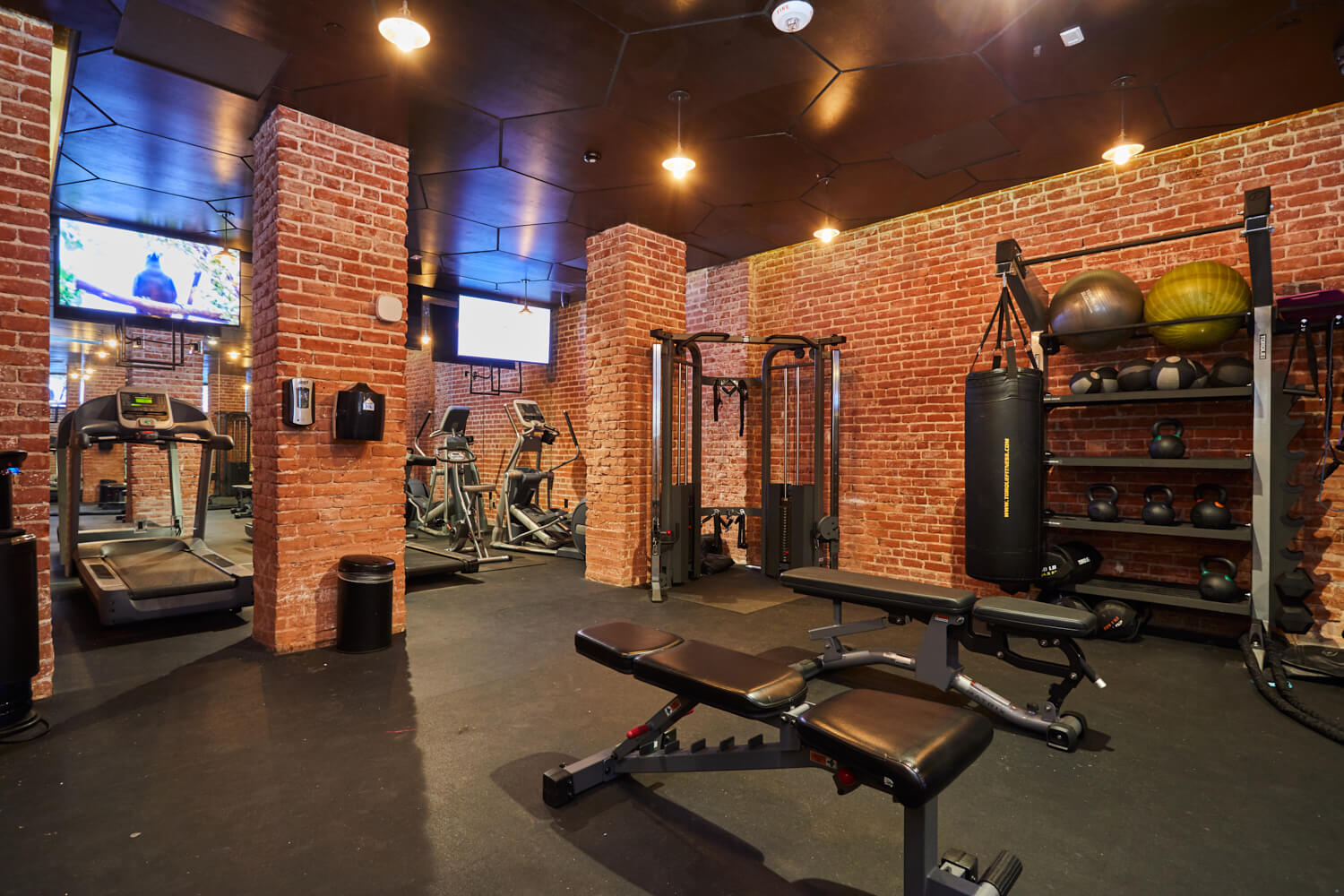 Exposed brick walls with kettlebells on the rack next to weight benches and other exercise equipment in the gym